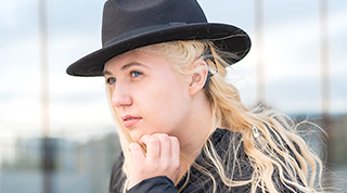 Une personne aux cheveux blonds coiffée d’un chapeau noir porte un appareil auditif à l’extérieur d’une succursale TD.