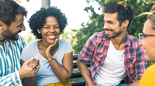 A diverse group of people laugh together while seated on a park bench. 