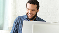 A Black business owner sits at a desk and reviews financial data with the aid of a calculator. 