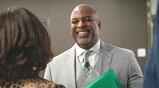 A middle-aged Black TD advisor in a business suit and green tie smiles as he speaks with a colleague.