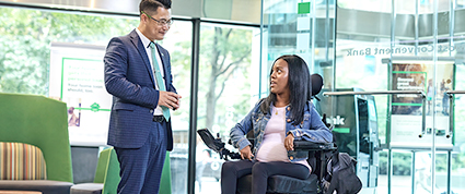 A male TD colleague greets a female customer that uses a  motorized wheelchair at a TD branch.