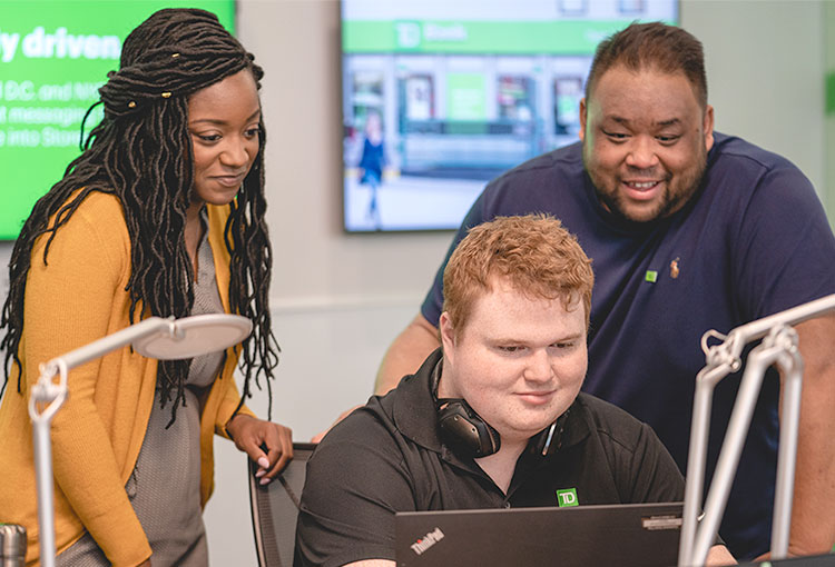 A racially diverse group of TD colleagues smile while looking at a laptop screen together.