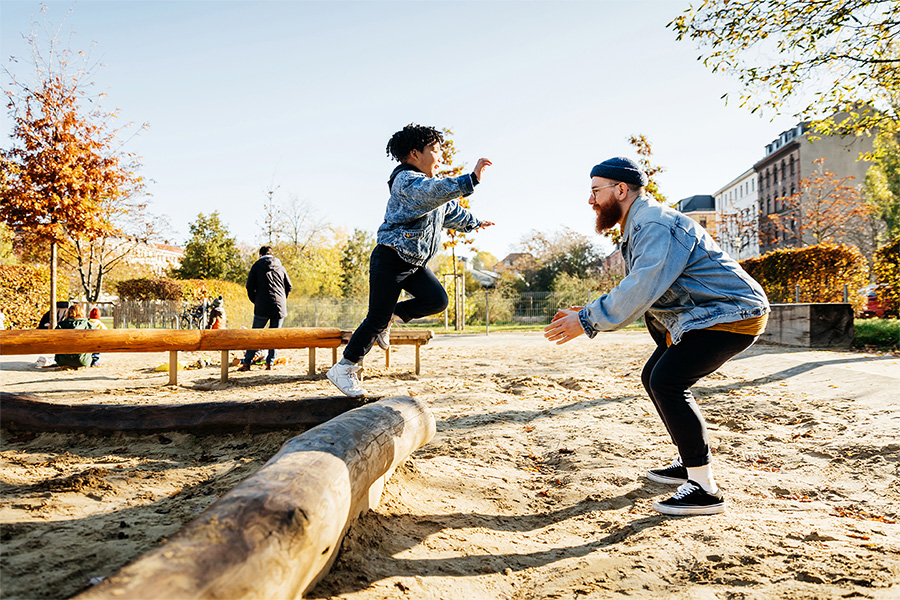 Young boy leaping into father's arms in playground