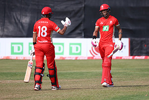 Two men on cricket pitch wearing cricket uniforms