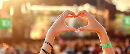 Heart hands sign at a music festival with a stage in the background