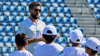 Man in black shirt teach 2 kids in white hats. 