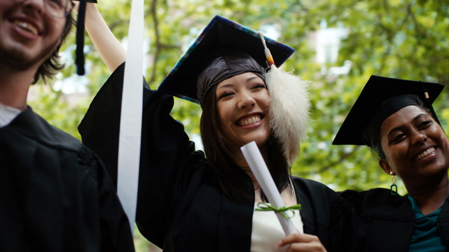 Woman from Indigenous community holding diploma high celebrates her graduation with friends.