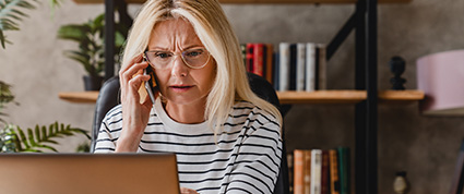 A lady looking at her laptop and talking on her mobile