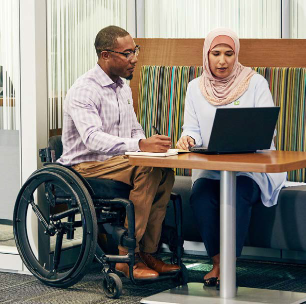 Un homme en fauteuil roulant est à côté d’une femme assise à une table; ils regardent ensemble l’écran d’un ordinateur portable