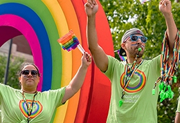 Des collègues de la TD portant des t-shirts verts et un maquillage arc-en-ciel distribuent des drapeaux et des sifflets de la Fierté du haut d’un char de la TD, à l’occasion d’un défilé de la Fierté.