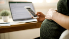 Une collègue de la TD enceinte portant une robe verte regarde son téléphone, la main posée sur son ventre.