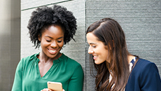 Deux collègues de la TD d’origines diverses regardent leur téléphone, debout à l’extérieur de leur bureau.
