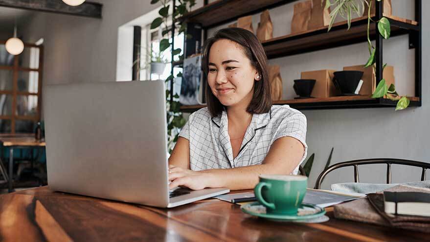 Une personne sourit alors qu’elle est assise et travaille sur un ordinateur portable dans un café. 