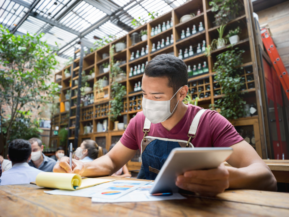 Man at work, sitting down looking at financial statements at a restaurant wearing a facemask