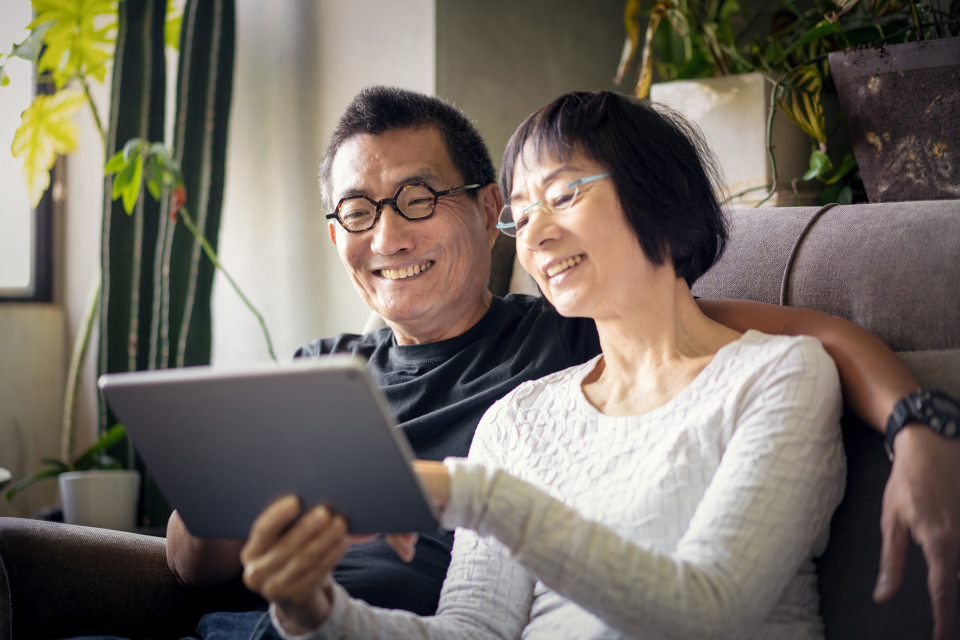 Un couple assis sur un canapé utilise une tablette