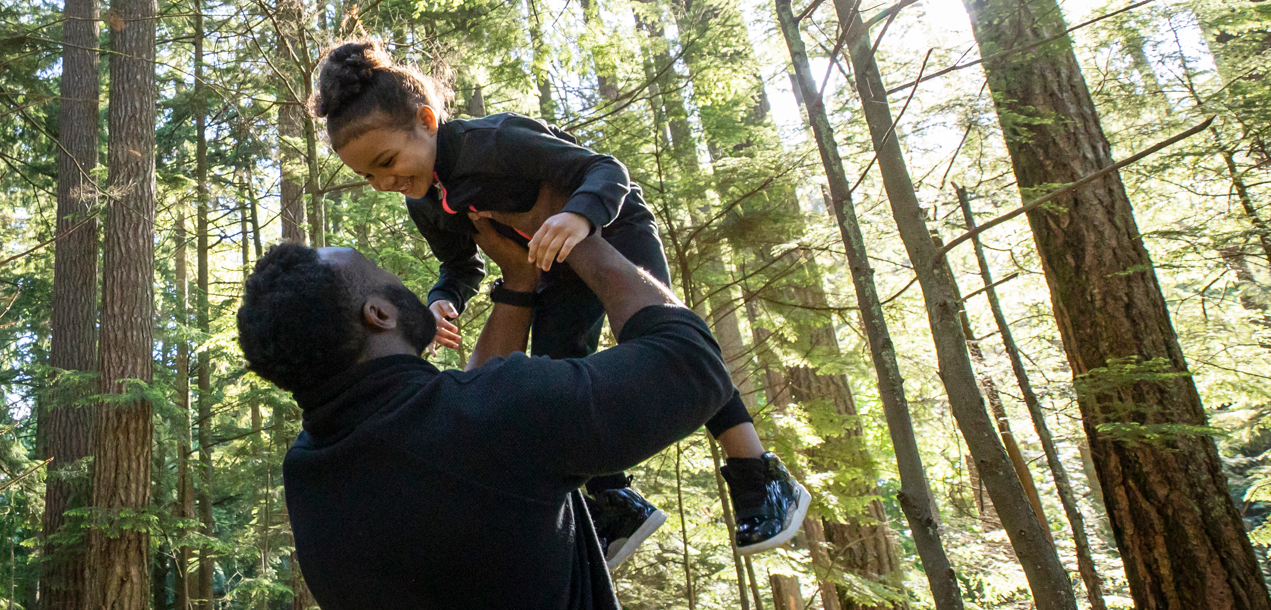 Dad lifting his smiling young daughter over his head at a park