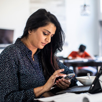Une femme d’affaires en télétravail utilise son cellulaire et son ordinateur portable tandis que des enfants participent à l’apprentissage en ligne en arrière-plan