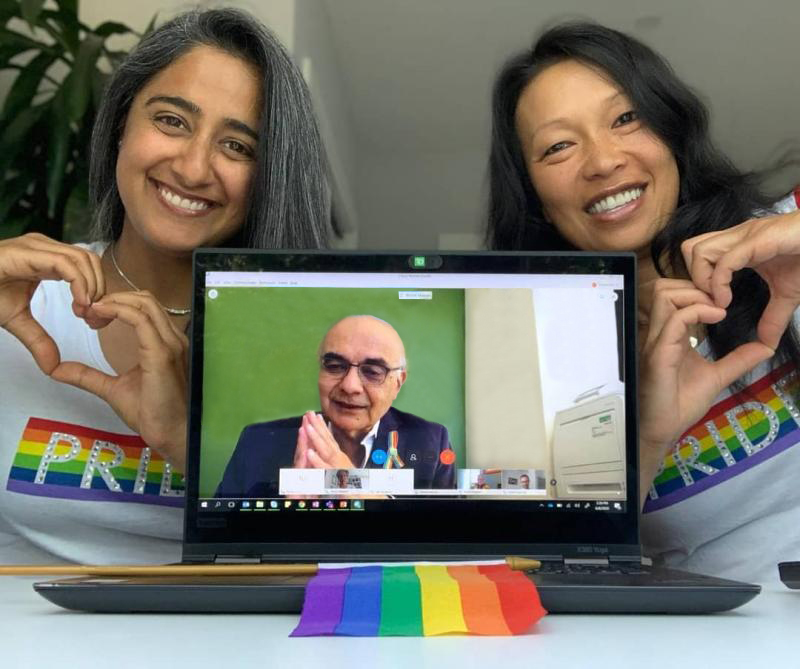 Photo de deux femmes participant à une activité virtuelle de la Fierté au moyen d’un ordinateur portable sur lequel on voit Bharat Masrani, président du Groupe et chef de la direction