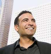 A smiling man stands in front of tall office buildings