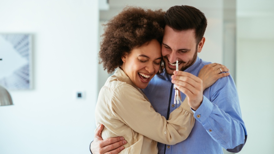 Two people smiling and hugging, holding a key to their home.